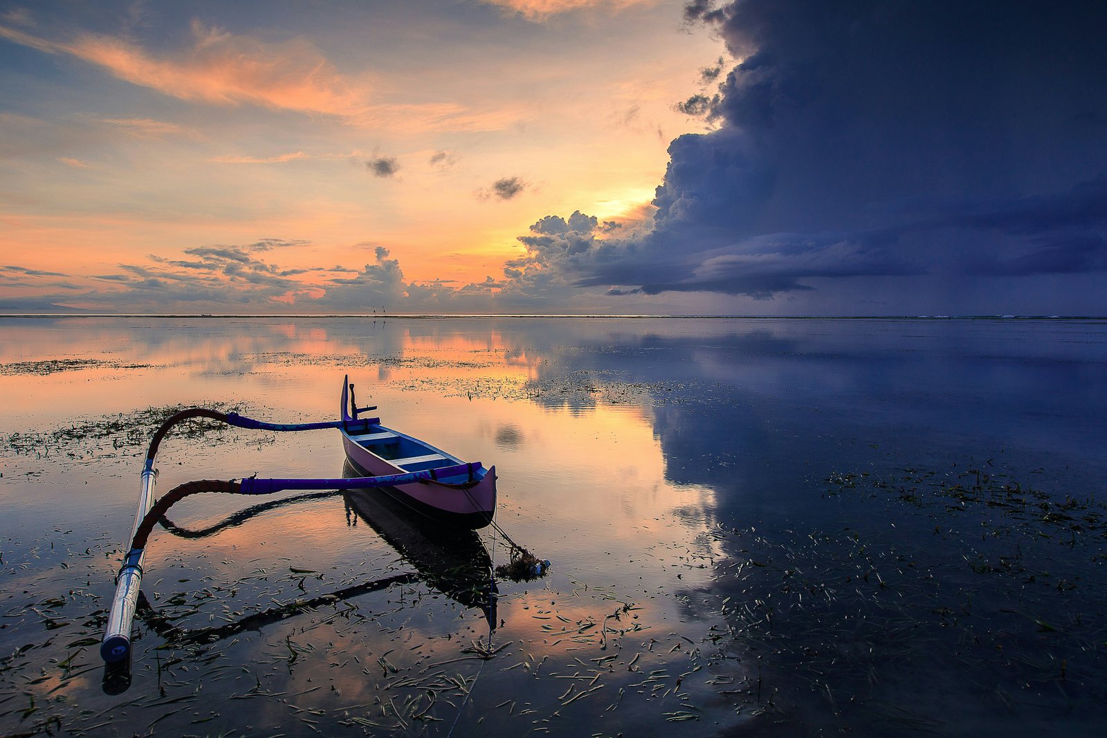 D'énormes nuages sombres en mer contrastant avec la lumière ailleurs. Un petit bateau en rangée est au premier plan sur la plage