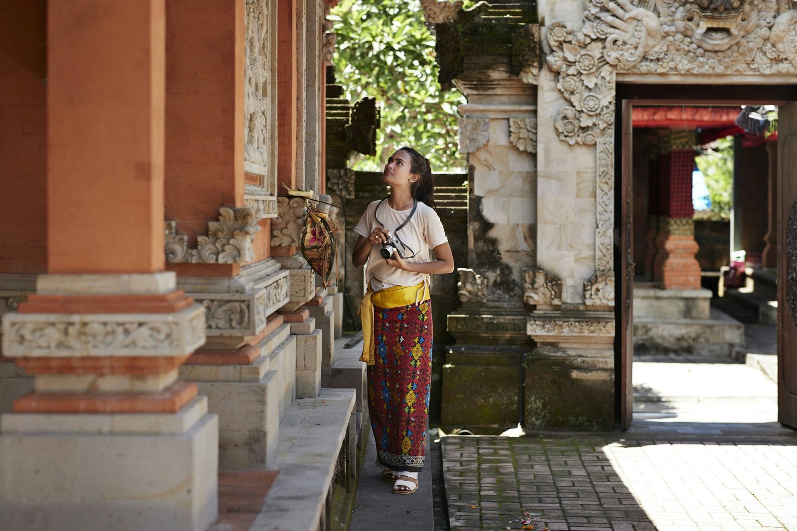 Un visiteur avec une caméra et portant un sarong regarde un détail architectural dans une cour du temple en Asie du Sud-Est