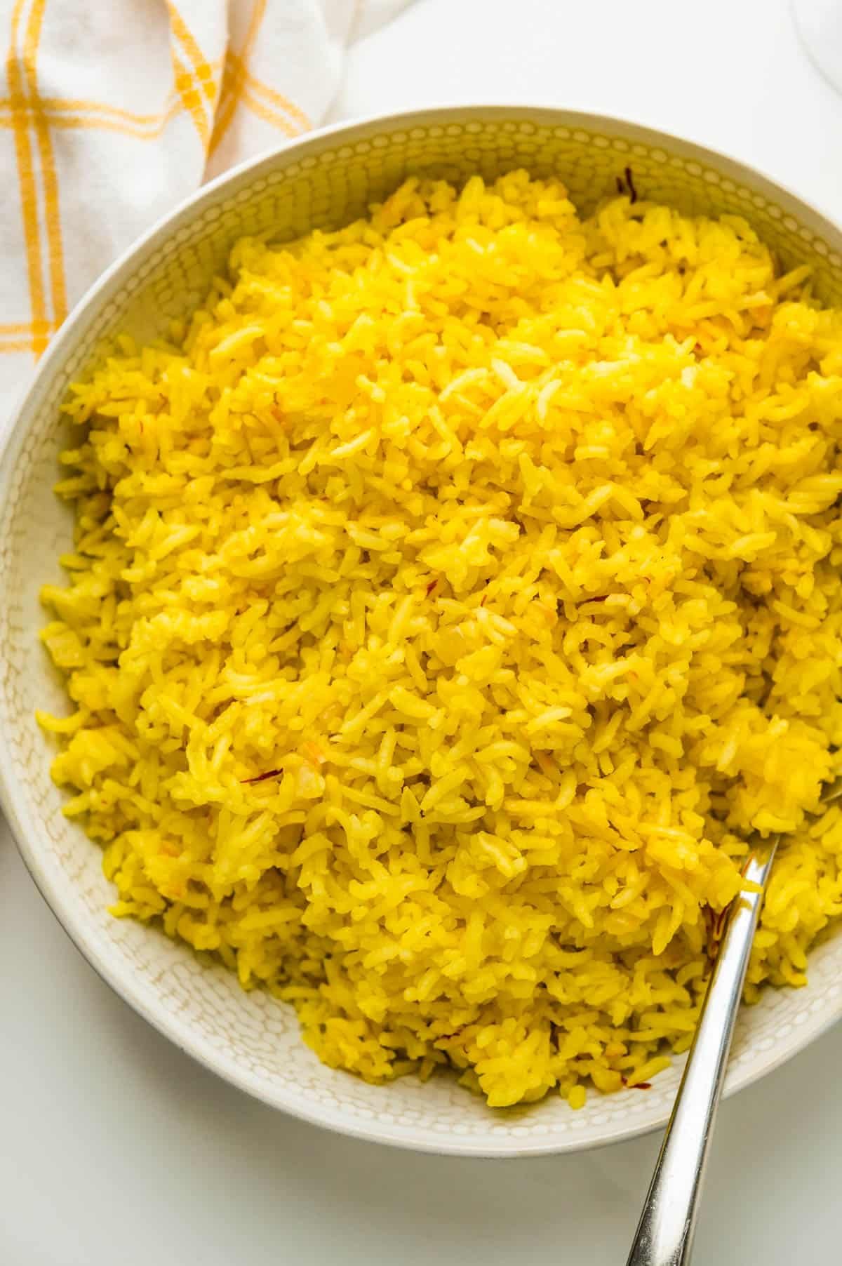 Un lot de recette de riz au safran jaune doré dans un bol blanc avec une cuillère.