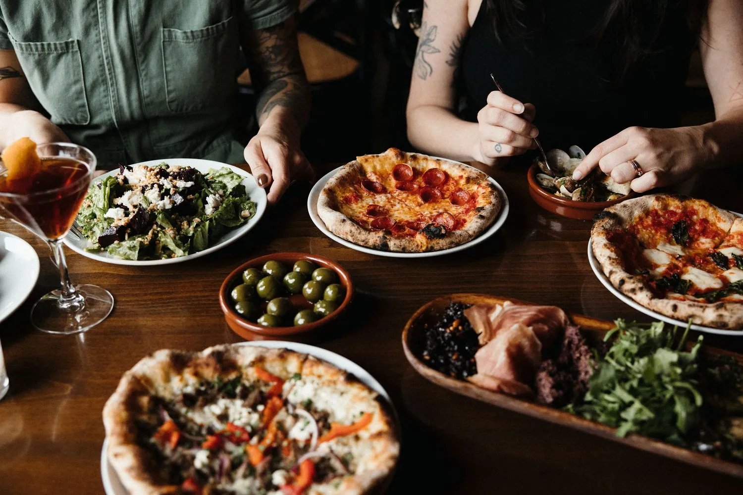 Deux convives sont assis à une table avec des pizzas tout autour, et d'autres plats italiens.