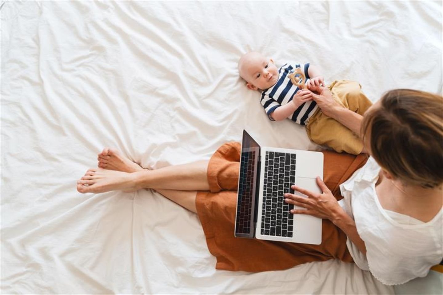 Mutter mit Baby and Laptop auf dem Bett beim Online-Shopping